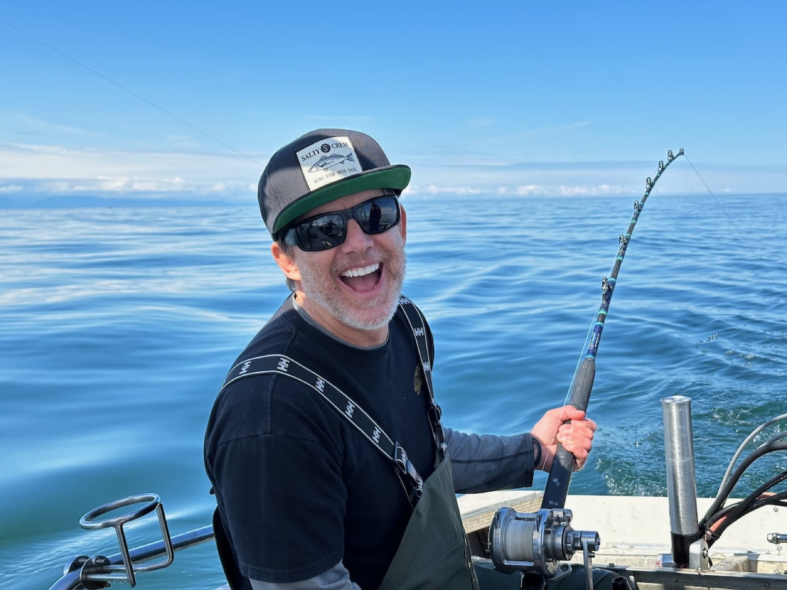 Pastor Woody on the charter — rod bent into a fight, big laughing smile, Cook Inlet behind