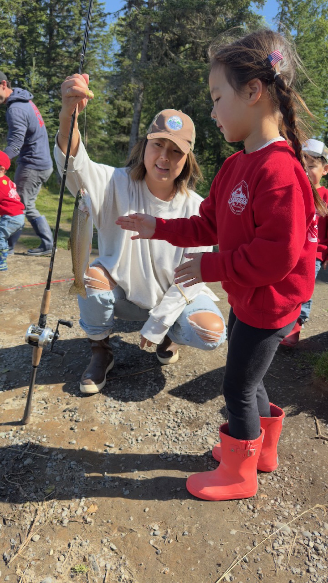 Janelle showing her daughter in red boots the fish dangling from the rod