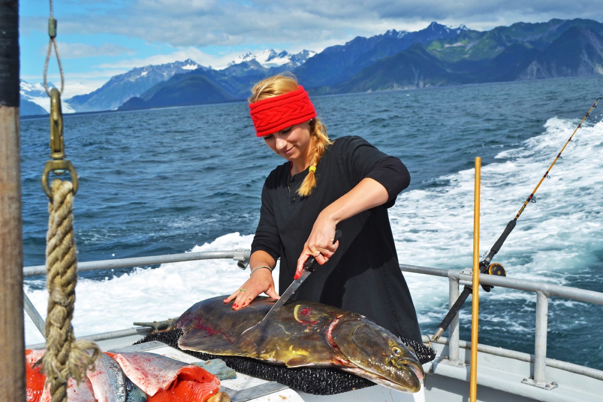 Joy Knepper filleting halibut on the boat, Kenai mountains behind
