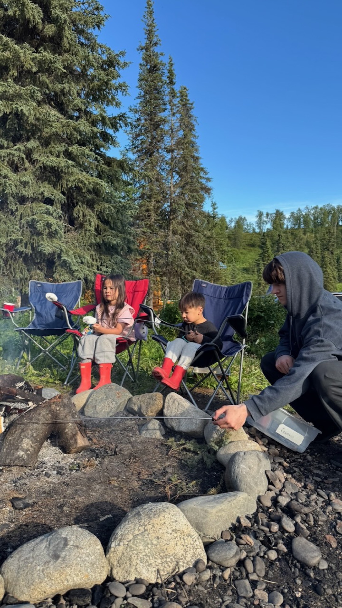 Two kids in red boots at the firepit, dad lighting marshmallows